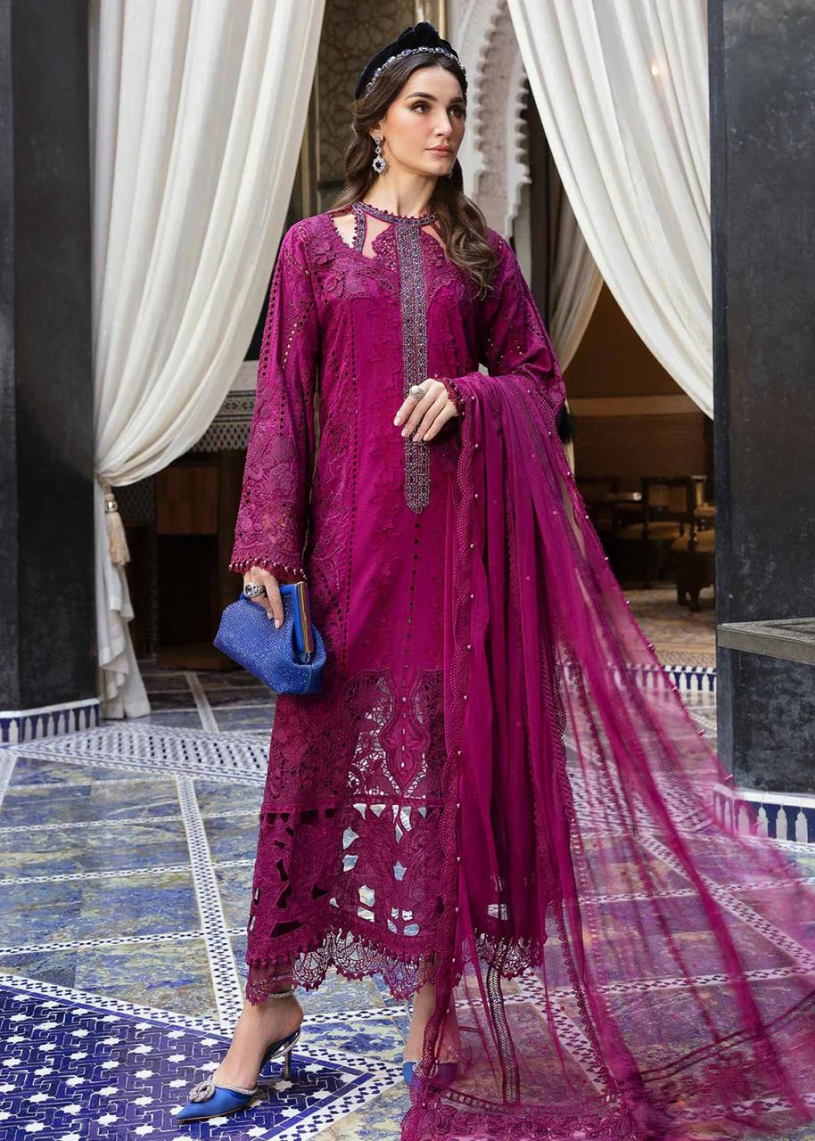 Woman in a vibrant pink traditional outfit with intricate patterns, standing in an elegant interior setting.
