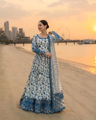 Woman in a blue and white floral dress standing on a beach at sunset.