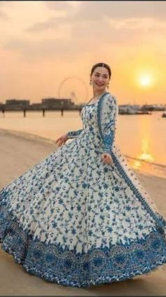 Woman in a blue and white dress standing on a beach at sunset.